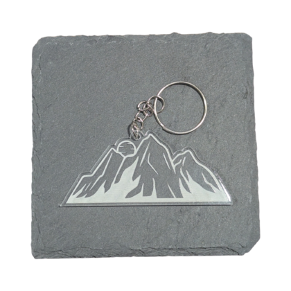 small clear engraved keychain of a mountain range with a sunrise peaking over the top displayed on a piece of slate for contrast