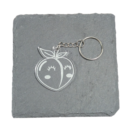 small clear engraved keychain of kawaii peach displayed on a piece of slate for contrast