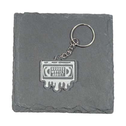 Horror Movies Addict VHS tape keychain displayed on slate for contrast